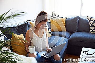 Young female working on tablet computer sat on sofa Stock Photo