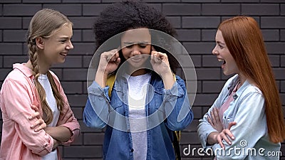 Young females mocking black classmate, bullying victim closing ears, conflict Stock Photo