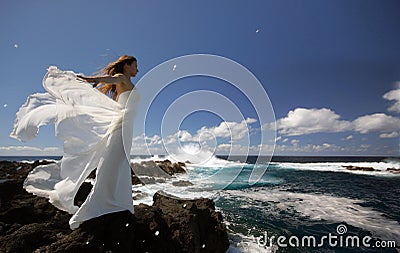 Young fiancee with white wings of wedding dress on rock sea shore on Sao Miguel island, Azores Stock Photo