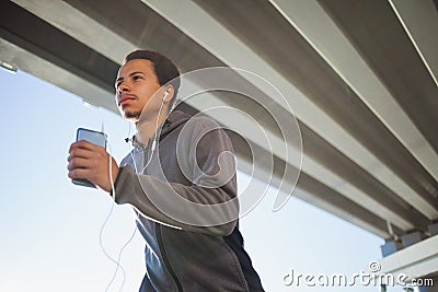 Young fit man running at outdoors, autumn and listening music, attractive dark skinned runner jogging fast, sport Stock Photo