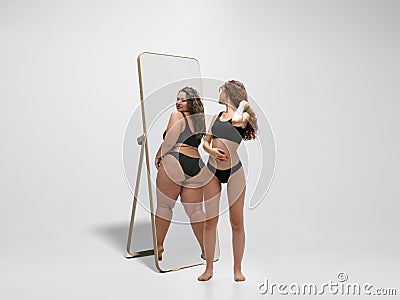 Young fit, slim woman looking at fat girl in mirror`s reflection on white background Stock Photo