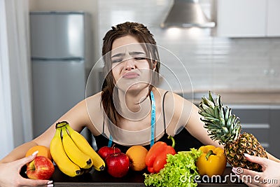 Young fit woman with centimeter round neck wearing black sports top standing in the kitchen full of fruits looks upset dietology Stock Photo