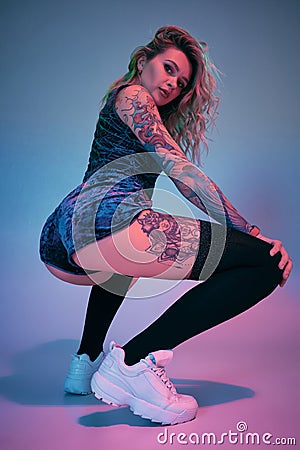 Young fitness blonde woman wearing blue velour booty shorts posing on camera, making squats in studio Stock Photo