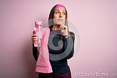Young fitness woman wearing sport clothes and towel drinking water from take away bottle serious face thinking about question, Stock Photo