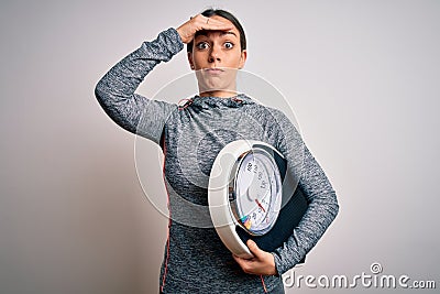 Young fitness woman wearing sport workout clothes holding scale for healthy weight stressed with hand on head, shocked with shame Stock Photo
