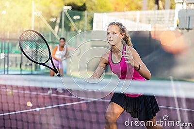 Young forcefully teenage girl playing tennis close to net on court Stock Photo