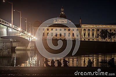 Young French people sitting on riverbank of Quais De Rhone, facing Hotel Dieu & Pont de la Guillotiere bridge Editorial Stock Photo