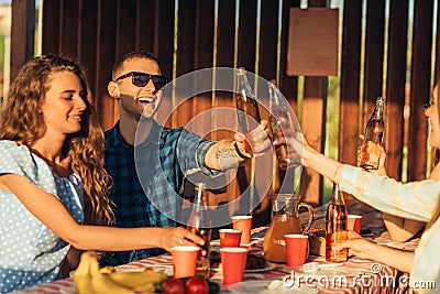 Young friends celebrate at sunset dinner, toast with drinks, happy people at terrace party eating barbecue Stock Photo