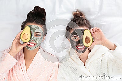 Young friends with facial masks fun on bed at pamper party, top view Stock Photo