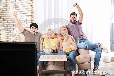 Young friends with snacks watching TV on sofa Stock Photo