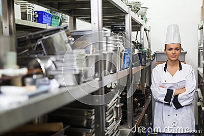 Young frowning chef standing arms crossed between shelves Stock Photo