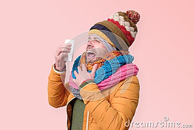 Young funny man in several hats ans scarfs man with handkerchief sneezing being ill. Stock Photo