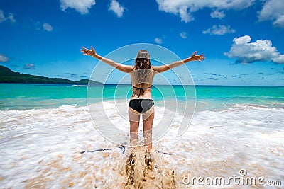 Young girl in bikini with raised arms greeting tropical sea and sun, on beach, freedom, vacation Stock Photo