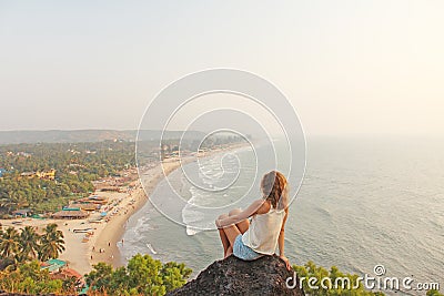 A young girl with blond hair sits on top of a mountain and looks Stock Photo