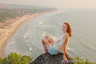 A young girl with blond hair sits on top of a mountain and looks Stock Photo