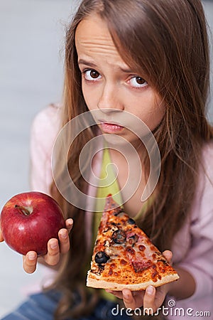 Young girl cannot decide between appetizing pizza and healthy apple Stock Photo