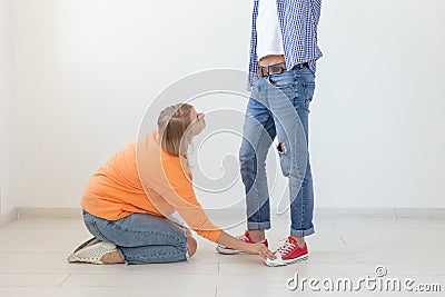 Young girl in casual clothes is sitting on her knees and touching the shoes of her domineering unidentified man posing Stock Photo