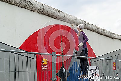 A young girl cleans the Berlin Wall, East Side Gallery, Berlin. Editorial Stock Photo