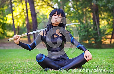 Young girl closed eyes, sitting on the grass with sword Stock Photo