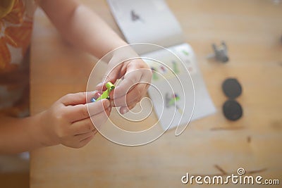 young girl in colorful dress puts togehter parts with her little fingers to build a toy tractor from plastic bricks Stock Photo