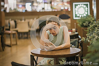 Young girl is crying along in a cafe closing her face with her hand. Teenager broke up with boyfriend Stock Photo