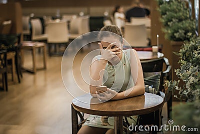 Young girl is crying along in a cafe closing her face with her hand. Teenager broke up with boyfriend Stock Photo