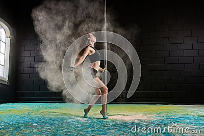Young girl is dancing at a pole at a hall with colorful floor background with a dust powder in motion Stock Photo