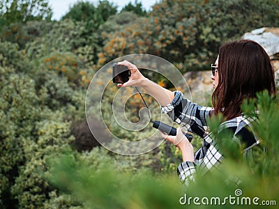 A young girl with dark hair, wearing glasses, takes photos of nature on her smartphone. The smartphone is charged from the power Stock Photo