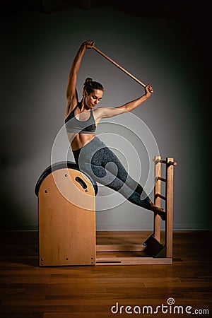 A young girl does Pilates exercises with a bed reformer, barrel machine tool. Beautiful slim fitness trainer on a Stock Photo