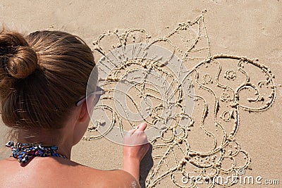 Young girl draws on the sand on the beach a zentangle, doodle. Stock Photo