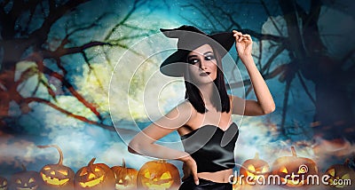 Young girl dressed as witch surrounded by spooky pumpkin heads in misty forest on full moon night. Halloween fantasy Stock Photo