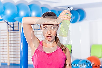 Young girl drinking isotonic drink, gym. She is wiping sweat Stock Photo