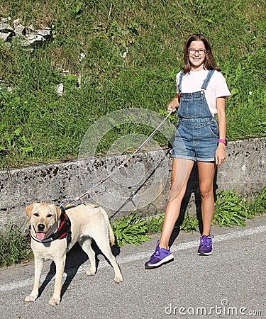 Young girl in dungarees walking the dog on a leash Stock Photo
