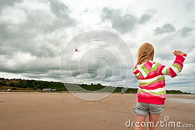 Young girl flying kite on beach with dramatic clouds in the background Stock Photo