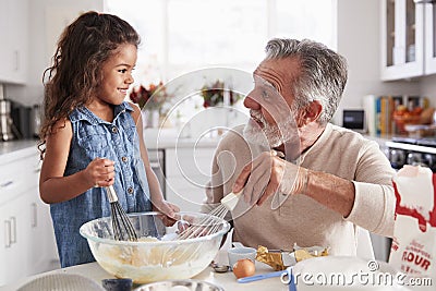 Young girl and grandfather making cake mixture at the kitchen table, smiling at each other, close up Stock Photo