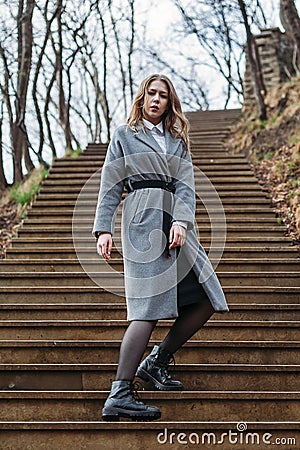 Young girl in gray coat posing on stairs in park on an autumn sunny day Stock Photo