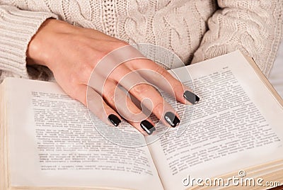 Young Girl hand with black nails holds book, woman in sweater reading book Stock Photo