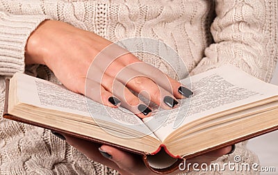 Young Girl hand with black nails holds book, woman in sweater reading book Stock Photo