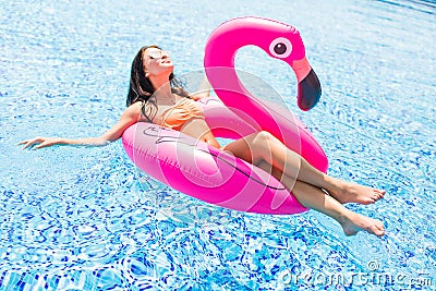 Young girl having fun and laughing and having fun in the pool on an inflatable pink flamingo in a bathing suit and sunglasses in s Stock Photo