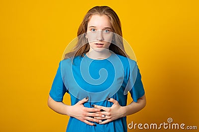 Young girl holding her stomach and frowns. Woman has a stomach ache. Female writhes in pain. Stock Photo