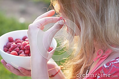Young girl holding a plate of raspberries, sitting on green grass, summer, dessert Stock Photo