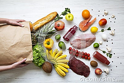 Young girl holds full paper bag of groceries on white wooden background. From above. Top view. Stock Photo