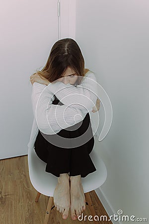 A young girl immersed in her thoughts sits on a chair on a white background, space for text. The concept of self-knowledge. Visual Stock Photo