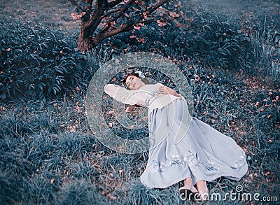 A young girl in a Japanese national kimono suit lies under a blooming sakura in pink petals. A Korean sleeping beauty Stock Photo