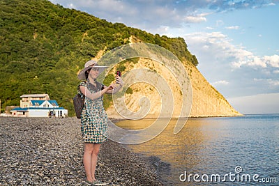 A young girl on a journey takes pictures on a mobile phone landscape, against the background of mountains and the sea Stock Photo