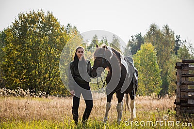 A young girl leads her horse by the bridle along a path along the fence Stock Photo