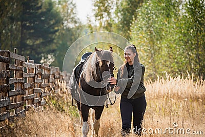A young girl leads her horse by the bridle along a path along the fence Stock Photo