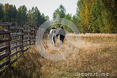 A young girl leads her horse by the bridle along a path along the fence Stock Photo