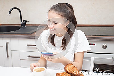 A young girl looks at a smartphone, communicates on social networks at breakfast Stock Photo
