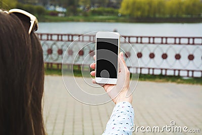 A young girl makes selfie in the park. A girl takes pictures of herself on a mobile phone in the street Stock Photo